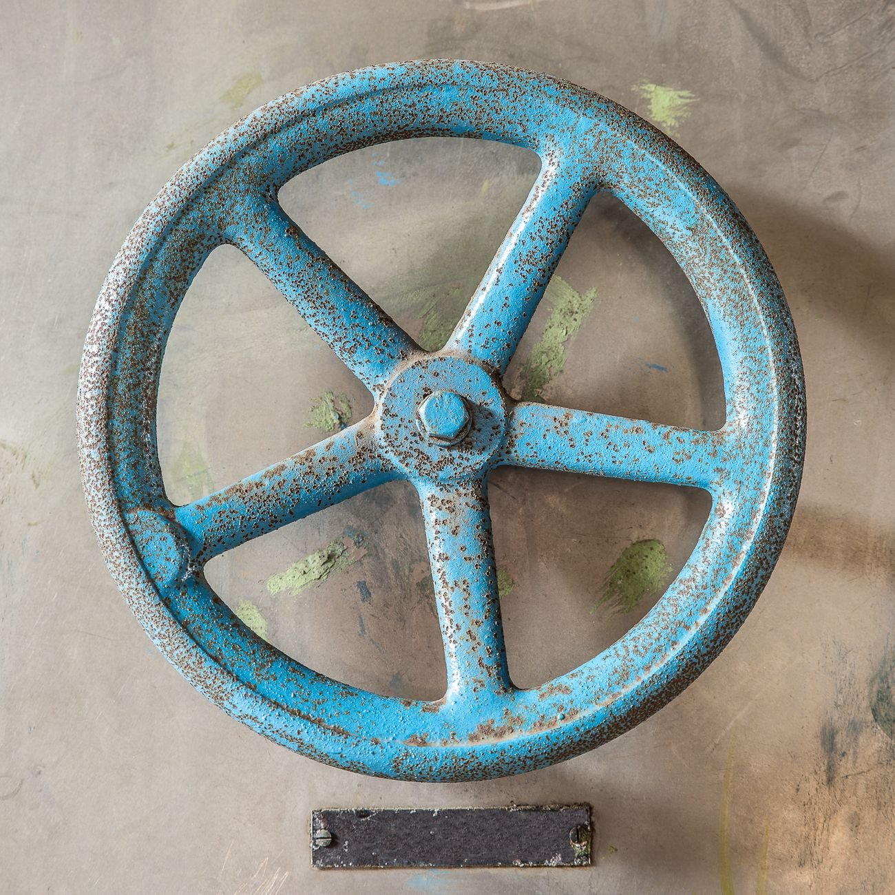 Close-up of a rusted blue metal wheel in an industrial setting, highlighting texture and color.